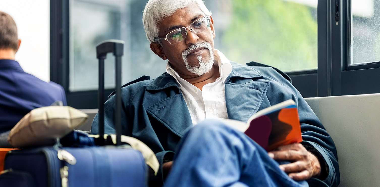 Older Indian man with white hair reading while in waiting room at airport