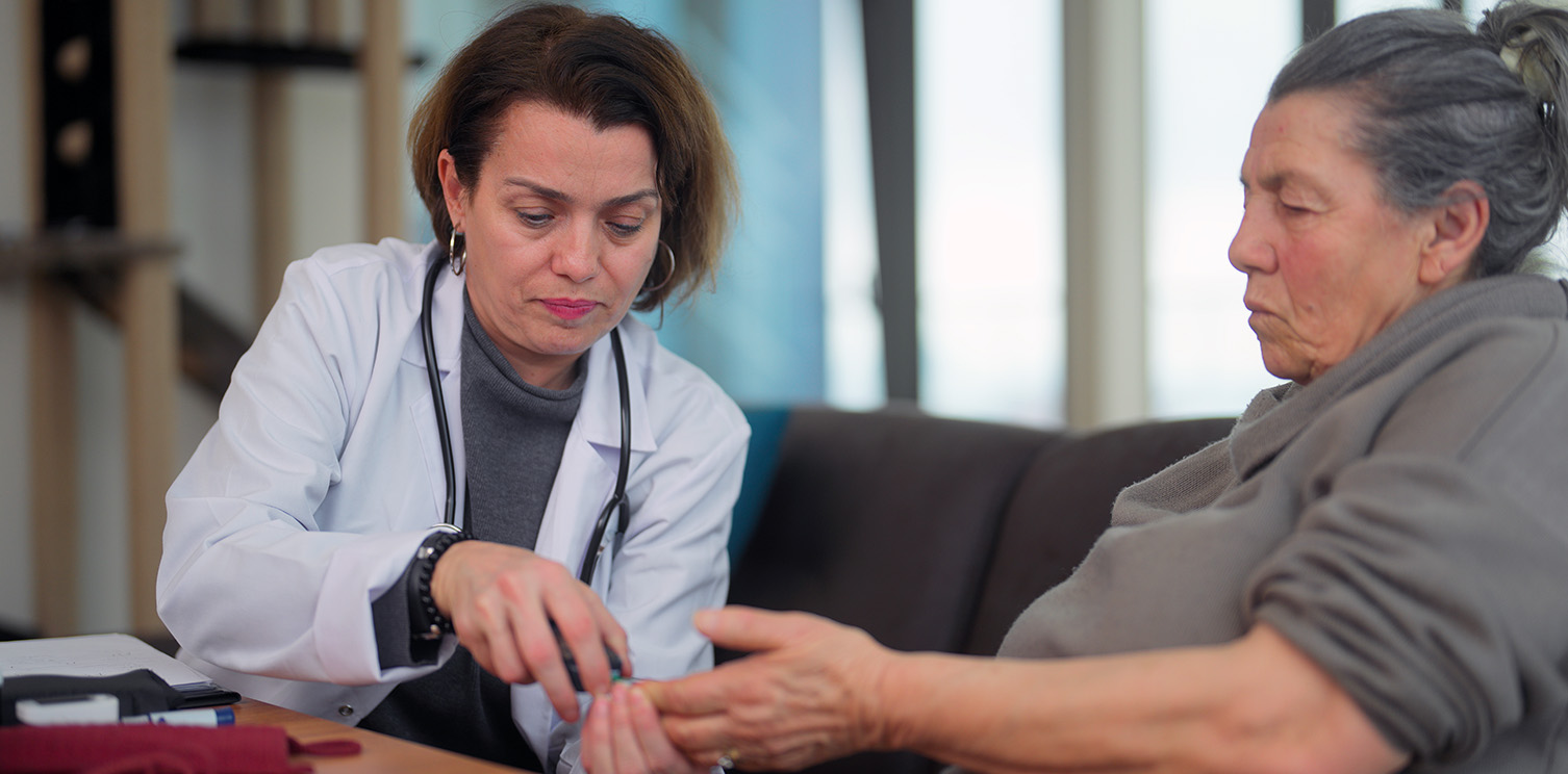 Female doctor checking female patient's blood sugar with finger prick