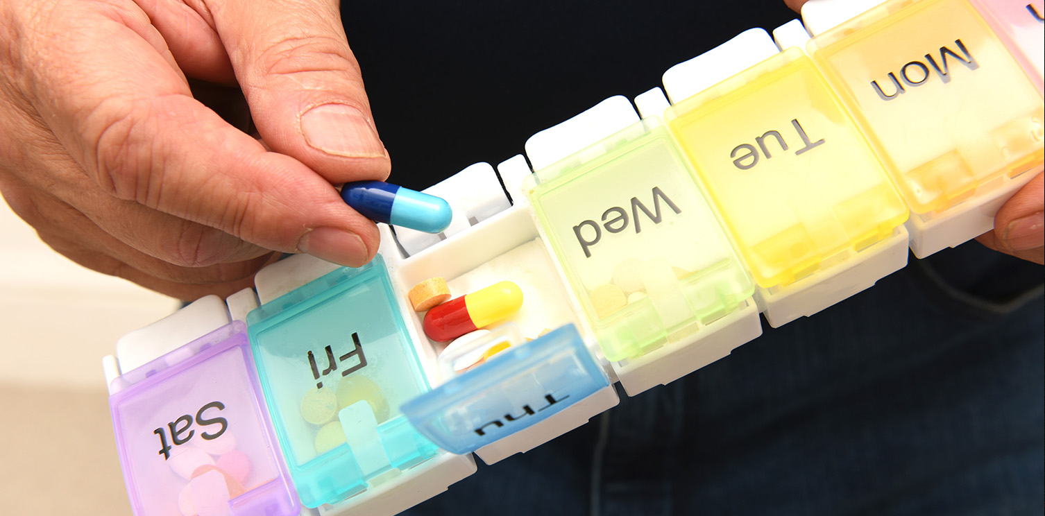 Hand holding pill over pill case with compartments for each day of the week