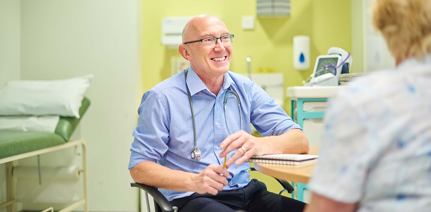 Older white man doctor, bald, smiling in an exam room