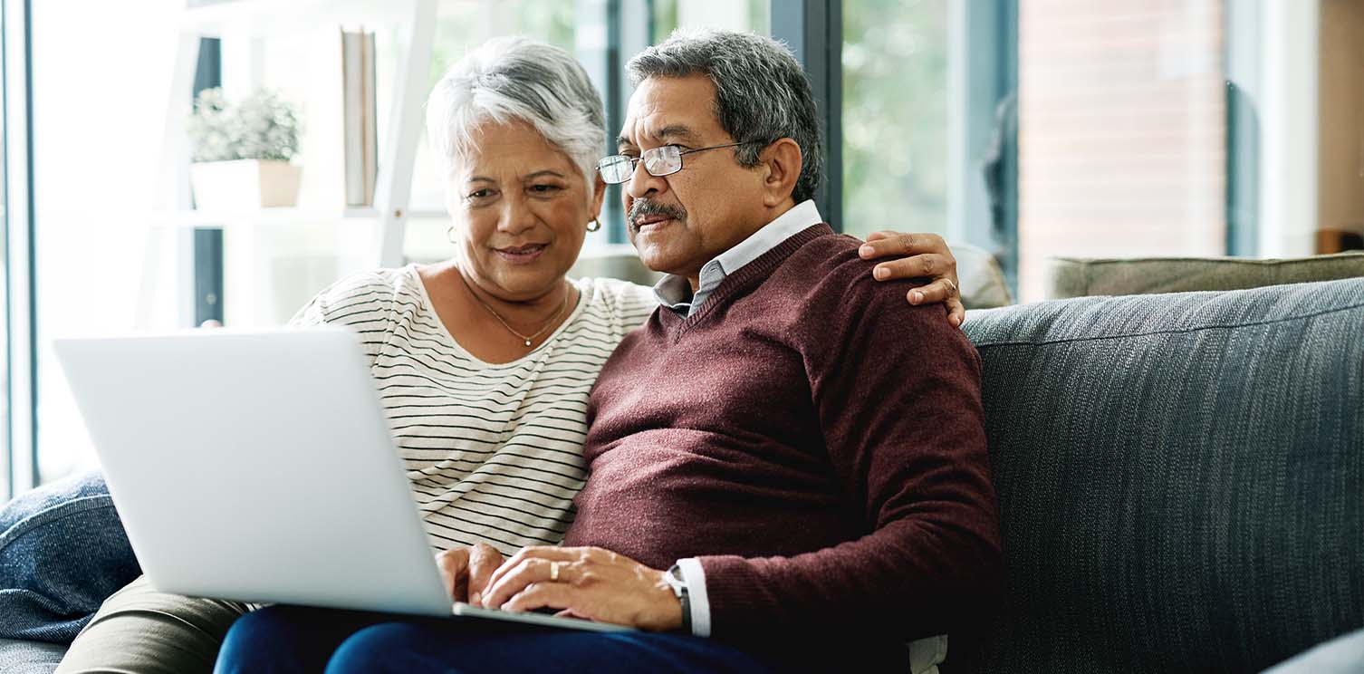 Older couple sitting on their couch while looking at a laptop 